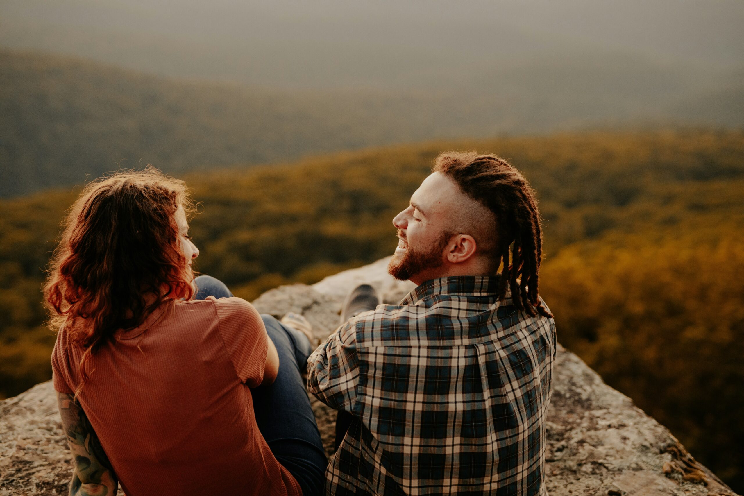 Couple sitting on a mountain ledge sharing laughter and connection, symbolizing deep emotional healing and renewal through therapy intensives with Heartsprout Therapy in Toronto and Vancouver.