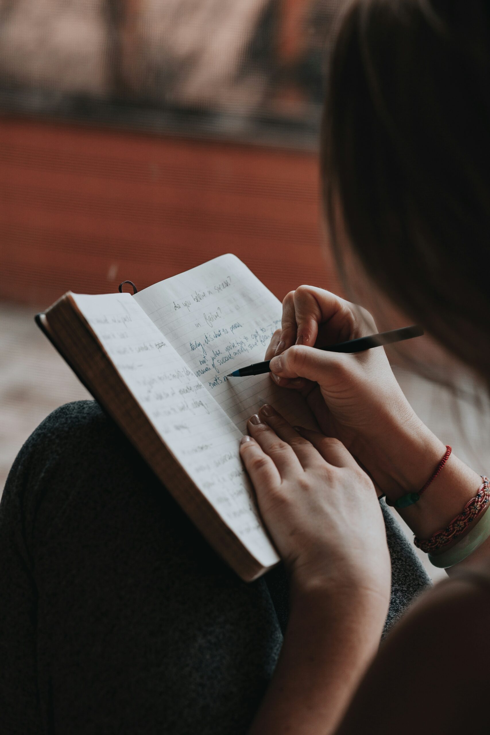 A person writing in a journal with a pen, seated comfortably with the notebook resting on their knees.