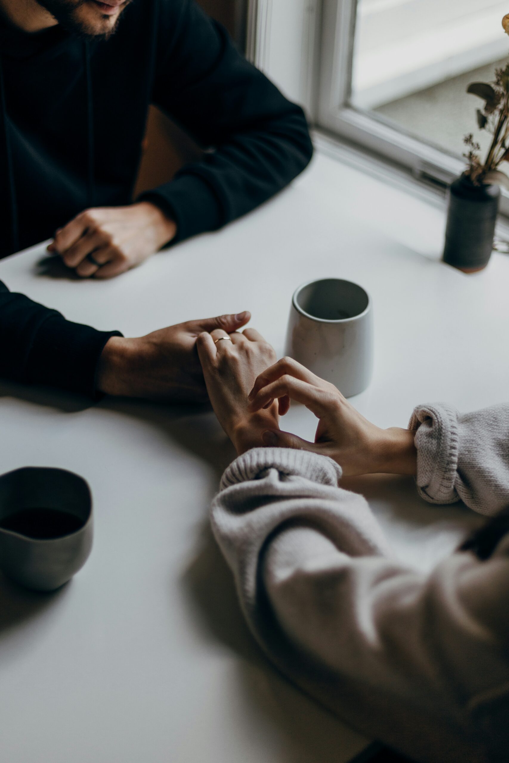Couple sitting across from each other at a table, holding hands during a quiet therapy conversation.
